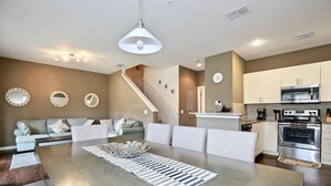 Eine moderne Küche mit Edelstahlgeräten, ein Essbereich mit einer zentralen Kochinsel und eine Treppe, die zu einer weiteren Ebene führt.