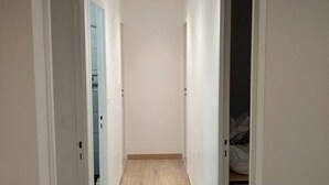 Un corridoio stretto con pareti bianche e pavimento in legno, che porta a una stanza con un armadio e un letto.