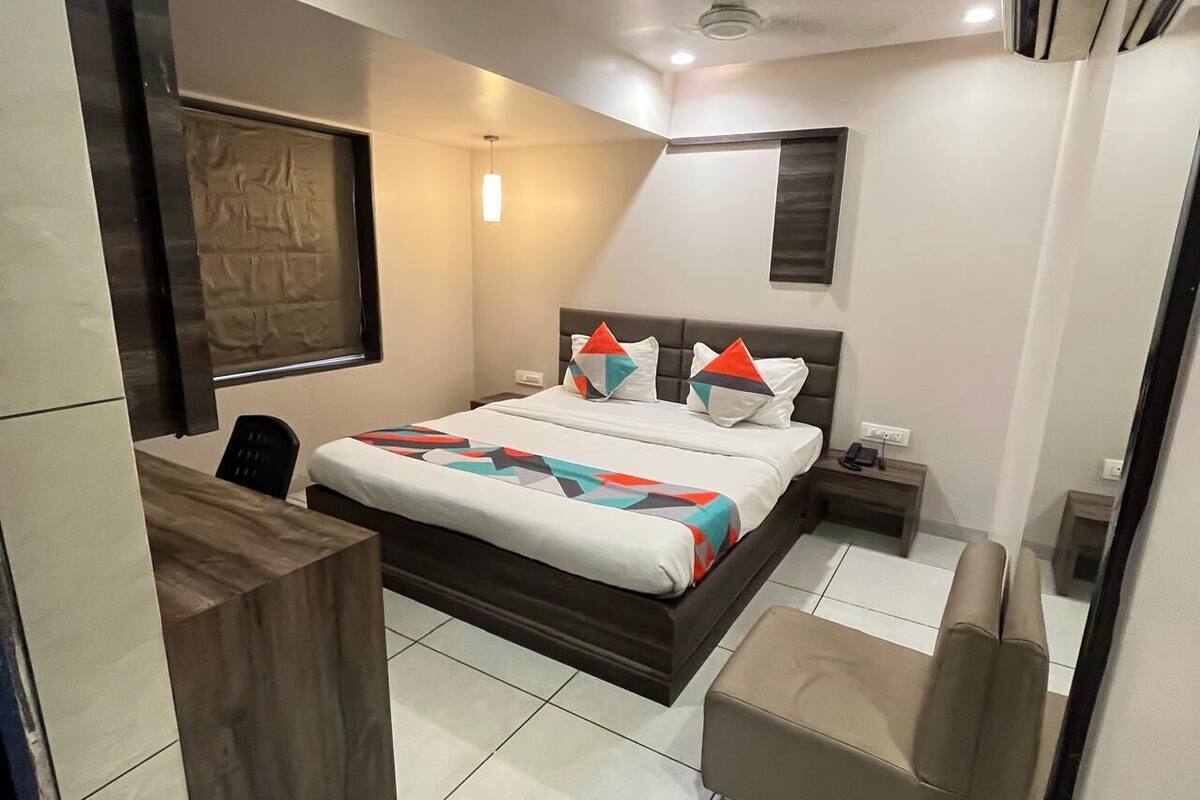 A modern hotel room with a bed, bedside table, chair, and a desk.