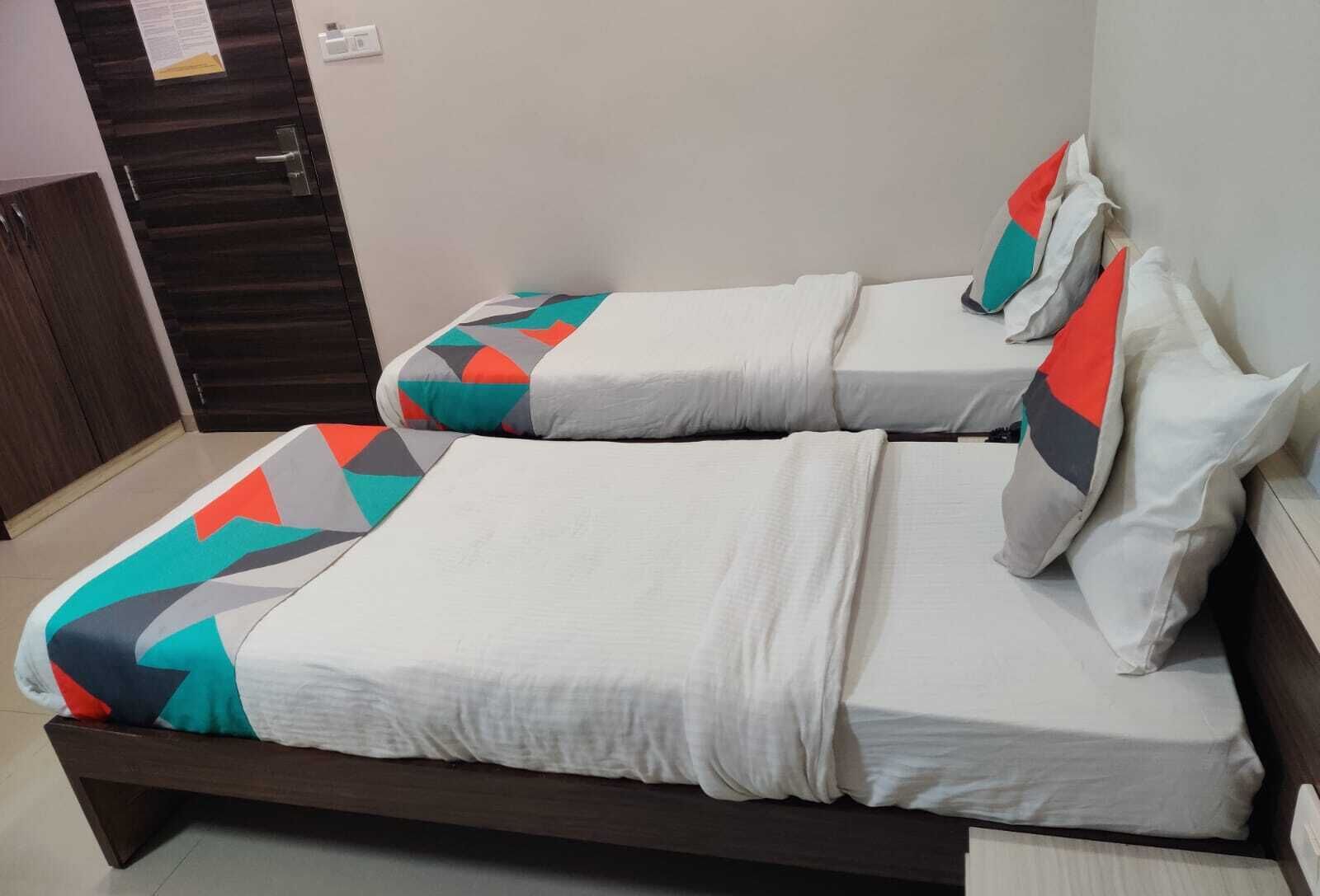 Een tweepersoonsbed met een sprei en kussens met een geometrisch patroon, een houten hoofdbord en een effen muur met een deur.