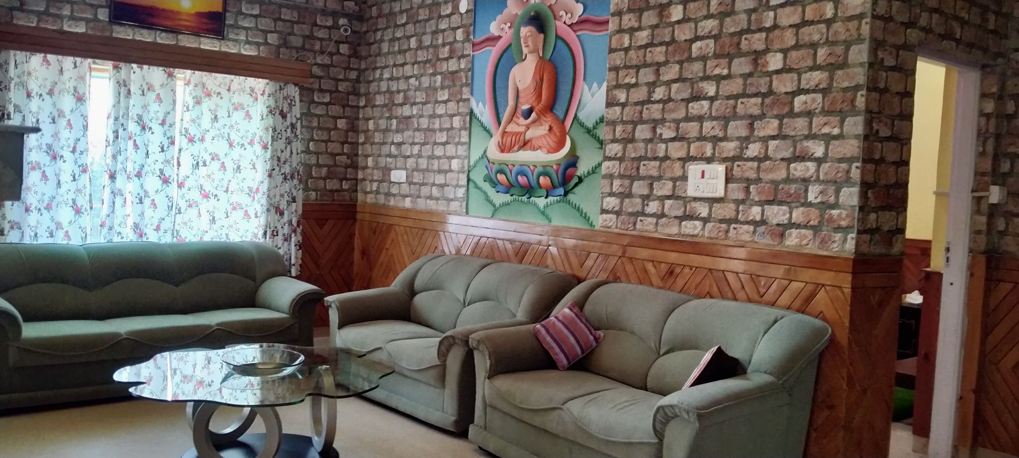 A room with a brick wall, a green sofa, a wooden bench, and a glass table.