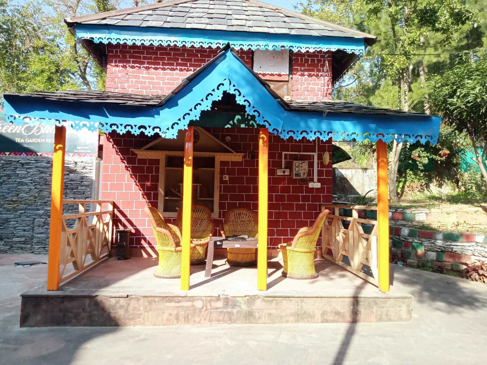 A brick building with a blue and yellow porch, wicker furniture, and a stone wall in the background.