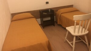 Una sistemazione modesta con una sola stanza, due letti singoli, un comodino in legno e una sedia bianca.