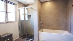 Een moderne badkamer met een douchecabine, een badkuip en een raam.