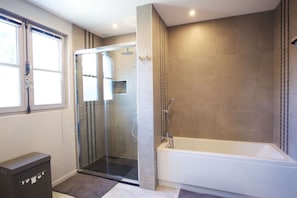 Un bagno moderno con doccia vetro-muraria, vasca e finestra.