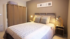 Une chambre à coucher avec un lit, deux lampes de chevet, une tête de lit, un tableau encadré au mur et un rideau.