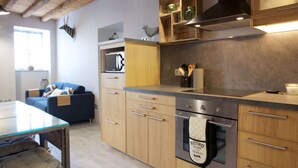 Une cuisine moderne avec des meubles en bois, un four encastré et un coin repas doté d’une table en verre.