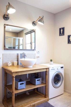 A bathroom with a wooden vanity, a large mirror, a sink, and a washing machine.