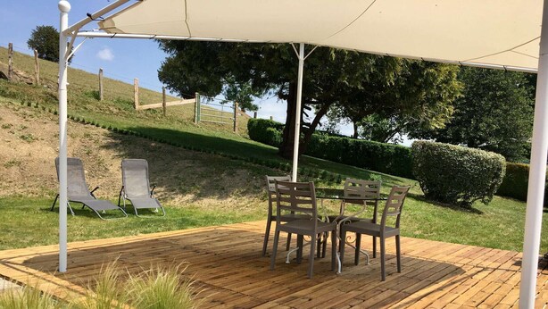 Une terrasse extérieure dotée d’une plateforme en bois, d’une table avec quatre chaises et d’un espace abrité sous une tonnelle blanche.