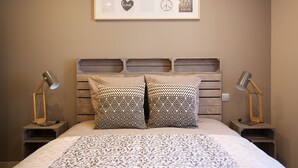 Een net opgemaakt bed met gekleurde kussens, een ingelijste afbeelding erboven en twee bedlampjes.