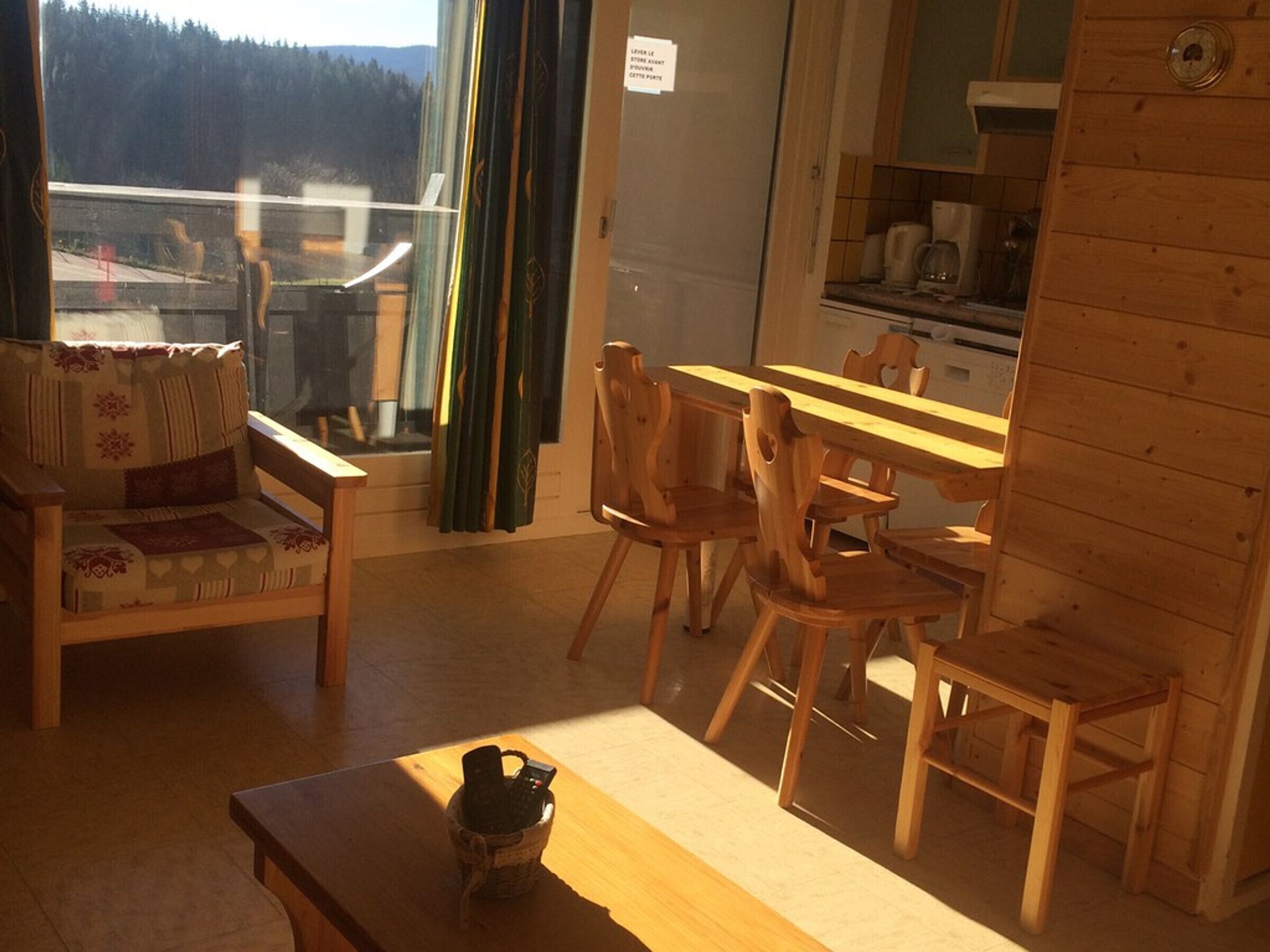Une pièce chaleureuse avec un canapé, des chaises en bois, une table et une vue sur une forêt, visible par la fenêtre.