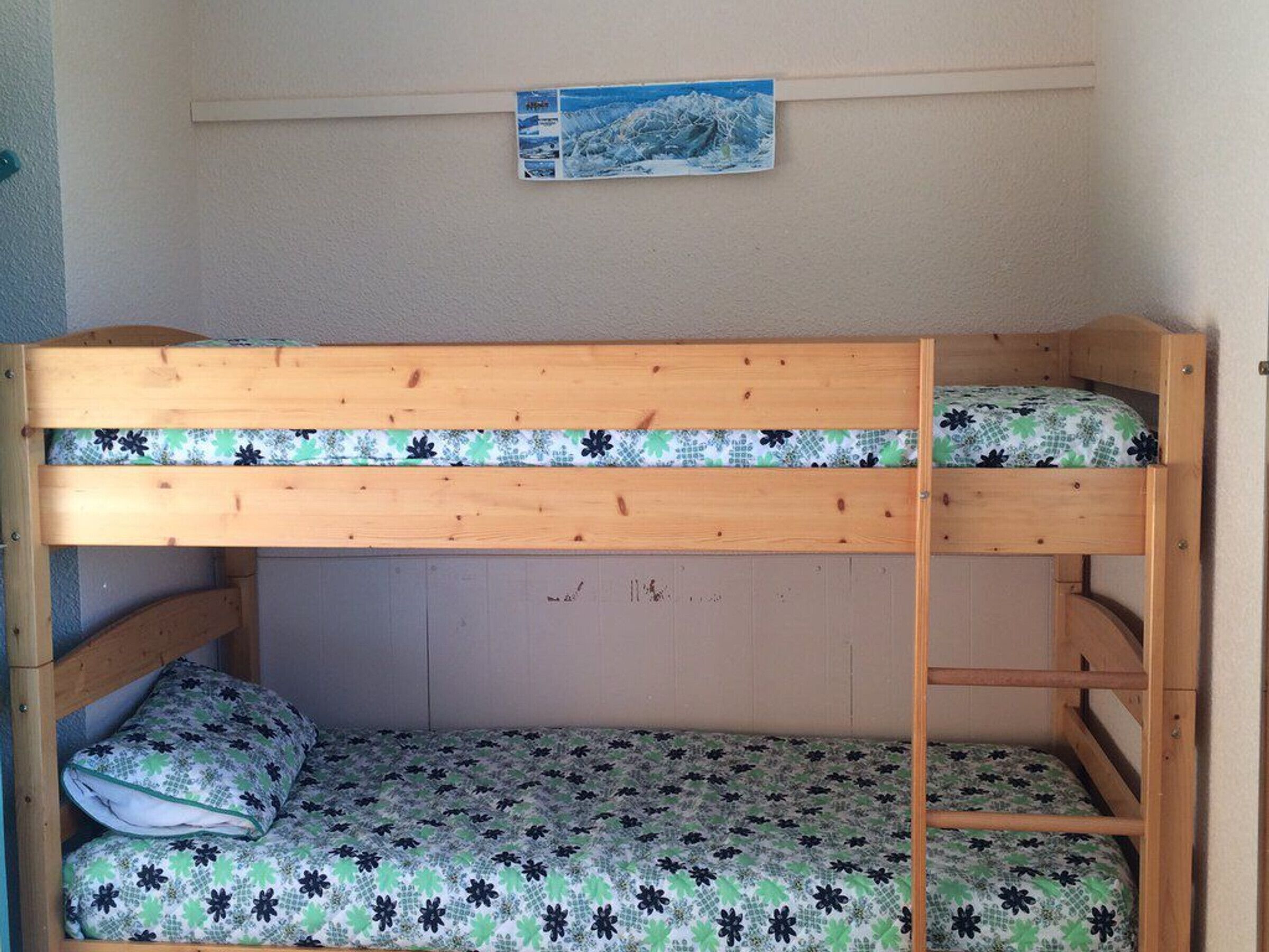 A bunk bed with floral bedding, a wooden headboard, and a small picture on the wall above.