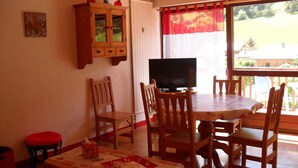Een eetgedeelte met een houten tafel, stoelen, een televisietoestel en een kast.