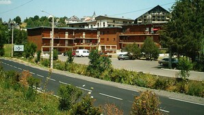 Een meerhoog hotel met een bakstenen gevel, meerdere balkons en een parkeerplaats met diverse auto's.