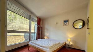 A bedroom with a bed, a window, a mirror, and a small bedside table. - Ski-in/ski-out apartment with balcony (Villard-de-Lans)