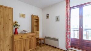 Una habitación con suelo de madera, armario empotrado, radiador y ventana con cortina.