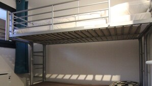 Une chambre avec un lit superposé, une échelle, un oreiller à carreaux et une fenêtre qui projette des ombres.