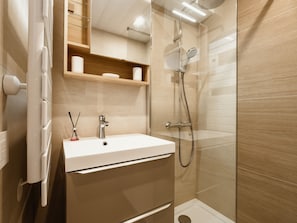 A modern bathroom with a glass-enclosed shower, a white sink, and a wooden shelf above the mirror.