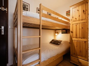 A bunk bed room with wooden headboard, a small shelf, and a cabinet.