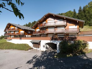 A multi-story hotel with balconies, a covered entrance, and a view of the surrounding greenery.
