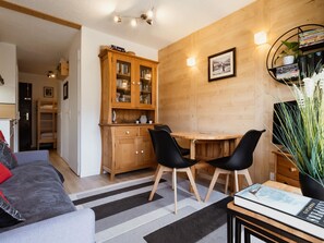 A cozy room with a wooden cabinet, a dining table with two chairs, a bookshelf, and a potted plant.