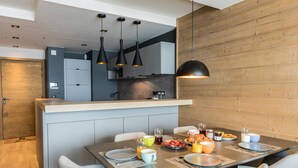 Una cocina moderna con una isla central, luces colgantes y un comedor con mesa lista para el desayuno.