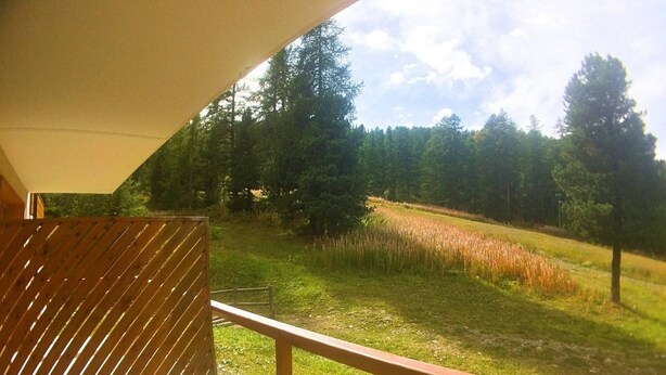 Een balkon met een houten spijlenhek met uitzicht op een grasveld en bomen.