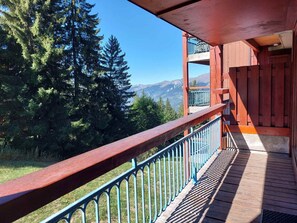 A wooden balcony with a metal railing overlooking a forested area and distant mountains.