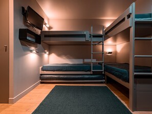 Une chambre avec un lit superposé, un téléviseur fixé au mur, un petit tapis sur le sol et une porte sur le côté gauche.