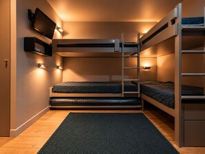 A bunk bed room with a television, wall-mounted lights, and a dark rug.