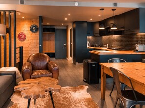 A modern kitchen with dark cabinets, a wooden dining table, and a leather armchair. - Renovated duplex, near slopes - 8 guests (Les Arcs 1800)