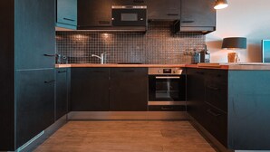 A modern kitchen with dark cabinetry, a tiled backsplash, stainless steel appliances, and pendant lighting.