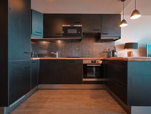 A modern kitchen with dark cabinetry, a tiled backsplash, and pendant lighting.
