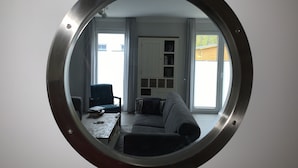 Un miroir rond reflétant un salon avec un canapé, un fauteuil, une table et une bibliothèque.