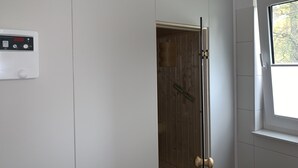 Une salle de bain avec un mur blanc, un thermostat, une porte en bois et une fenêtre donnant sur des arbres.