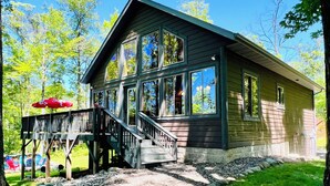 A wooden cabin with a deck and stairs leading to a covered porch area.