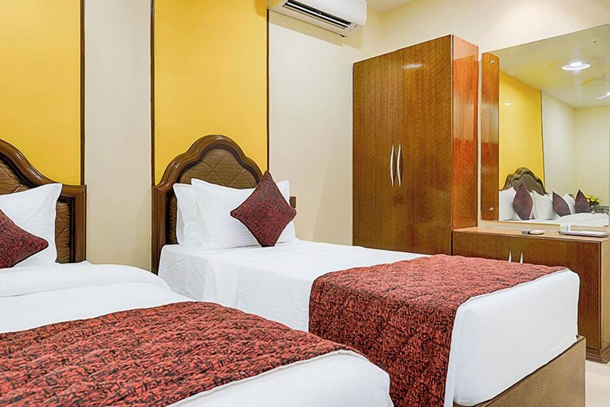 A hotel room with two beds, a wooden wardrobe, and a mirror.