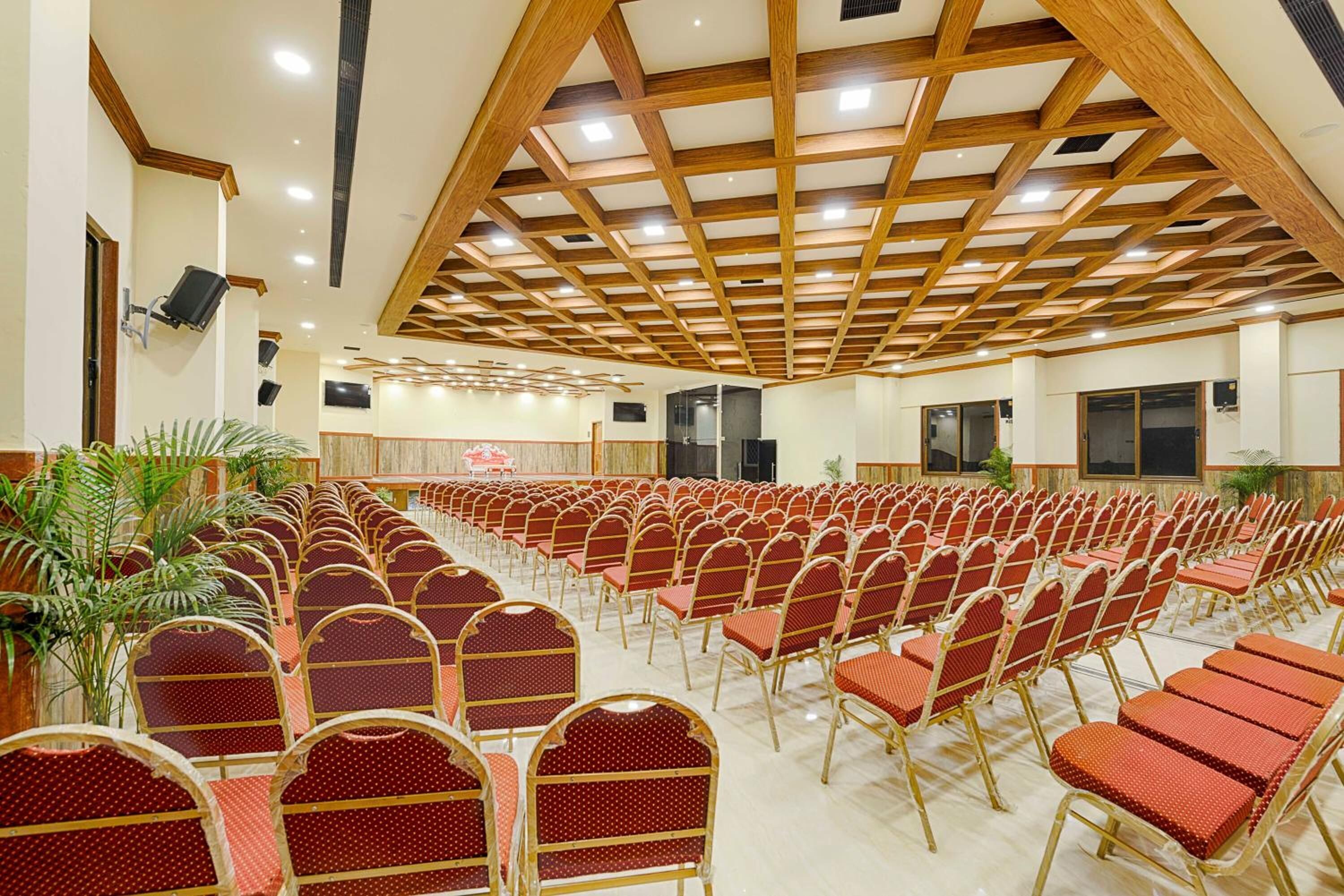 Une salle de conférence avec des rangées de chaises rouges, des poutres en bois au plafond et une estrade.