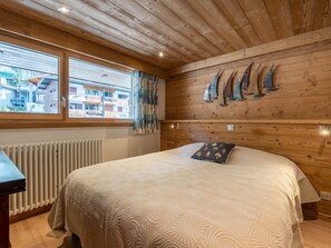 Quarto com painéis de madeira, uma cama, uma janela com cortinas e uma decoração náutica pendurada na parede.