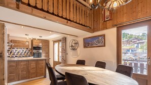 A modern kitchen with wooden cabinets, a dining area with a large table and chairs, and a view of a mountainous town through a large window. - Spacious 4-room flat, 6 pers., La Clusaz, large balcony (La Clusaz)