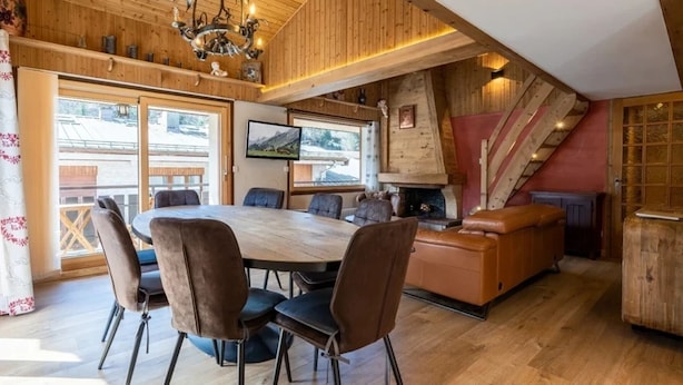 A spacious dining area with a large wooden table and chairs, a fireplace, and a staircase leading to an upper level. - Spacious 4-room flat, 6 pers., La Clusaz, large balcony (La Clusaz)