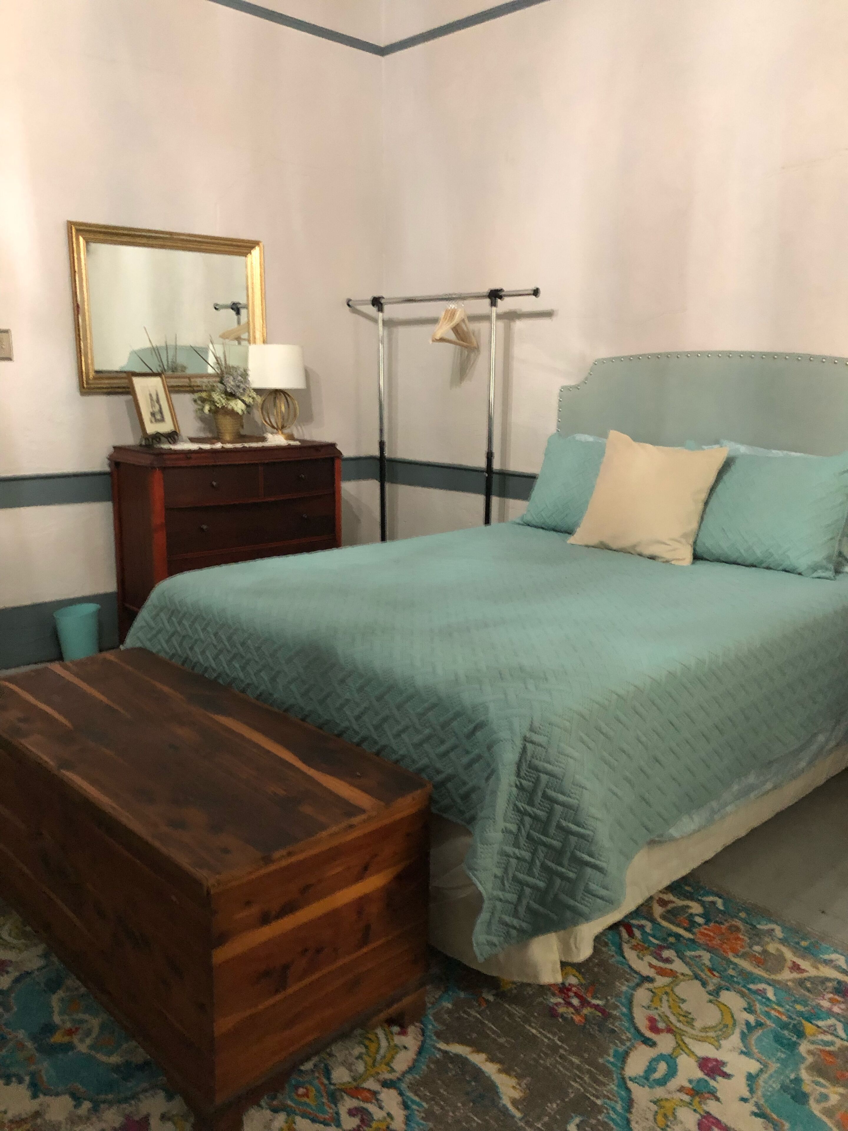 Ein Schlafzimmer mit einem Bett, einer Holzkiste, einem Schminktisch, einem Spiegel und einem Wäscheständer.