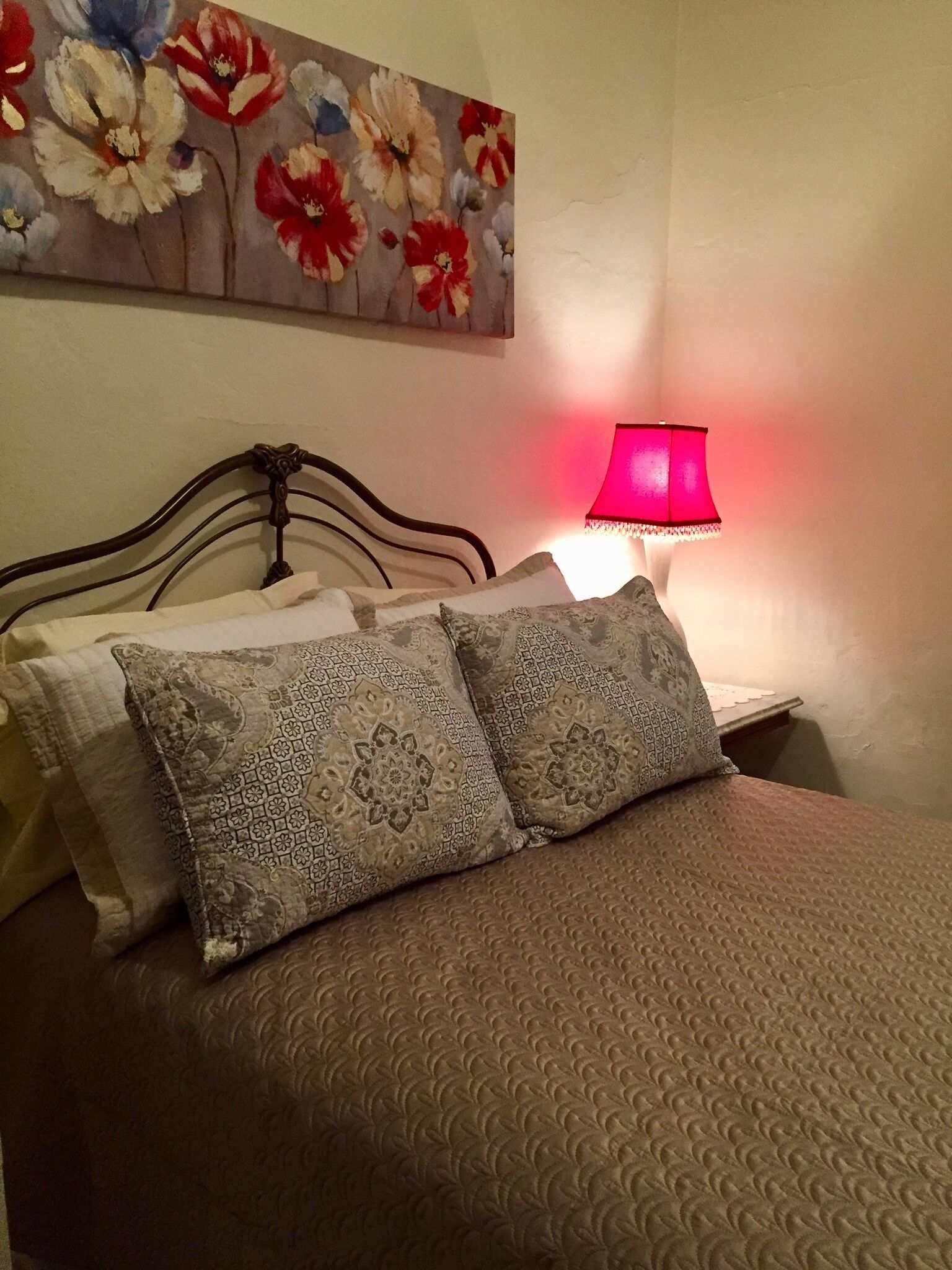 A bed with patterned pillows, a headboard, and a wall-mounted floral painting.