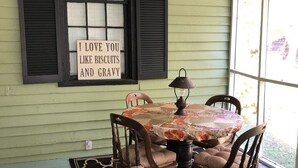 A dining area with a table set for four, a sign above the window, and a patterned rug on the floor. - In 1840 Burn Cottage (Society Hill)