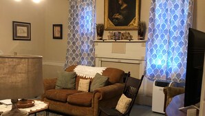 A living room with a brown sofa, a wooden rocking chair, a table with a vase, and a television. - In 1840 Burn Cottage (Society Hill)