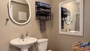 A bathroom with a white sink, toilet, and two mirrors with decorative frames. There are towels stacked on a rack and a basket with towels. - Prickly Pear Suite, Near Old Town (Albuquerque)