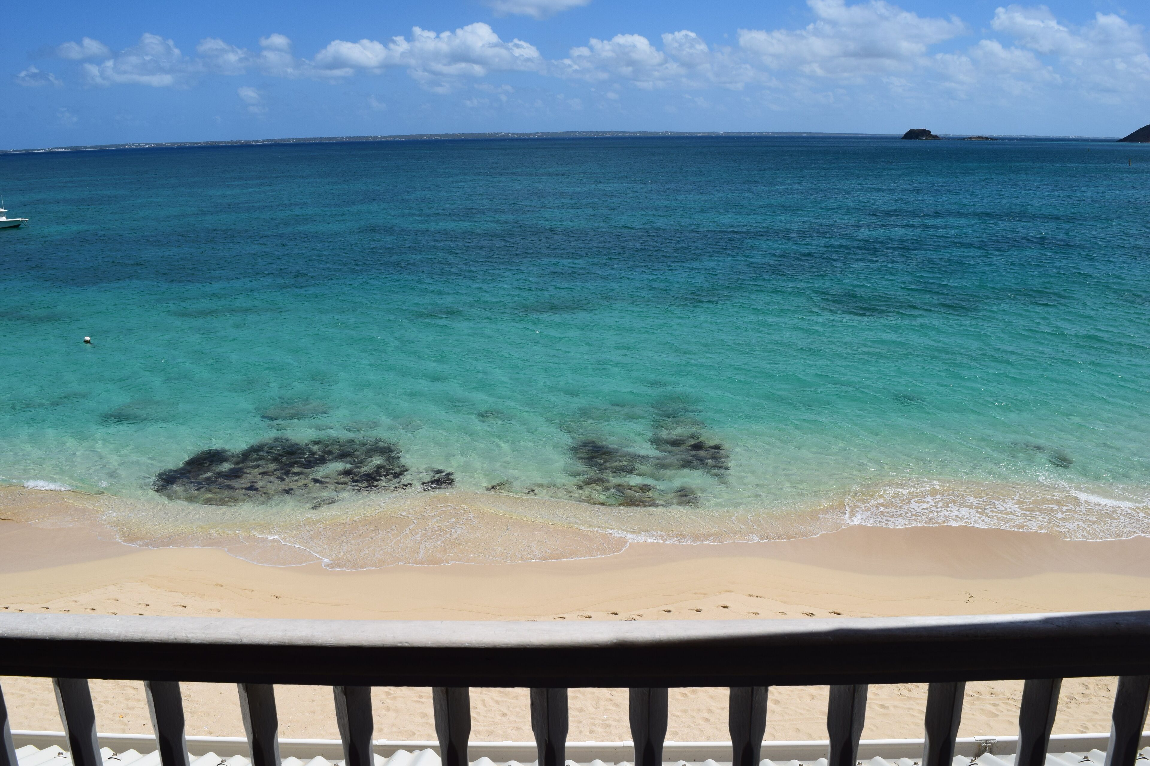 Une plage à l’eau turquoise et limpide, un rivage sablonneux et une île qui se dessine  à l’horizon.
