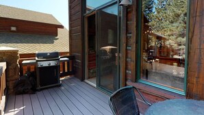 A wooden deck with a grill, a glass door leading to a covered area, and a table with a chair. - Stonegate #14 Luxury Cabin with Hot Tub - Walking Distance to Village & Gondola! (Mammoth Lakes)