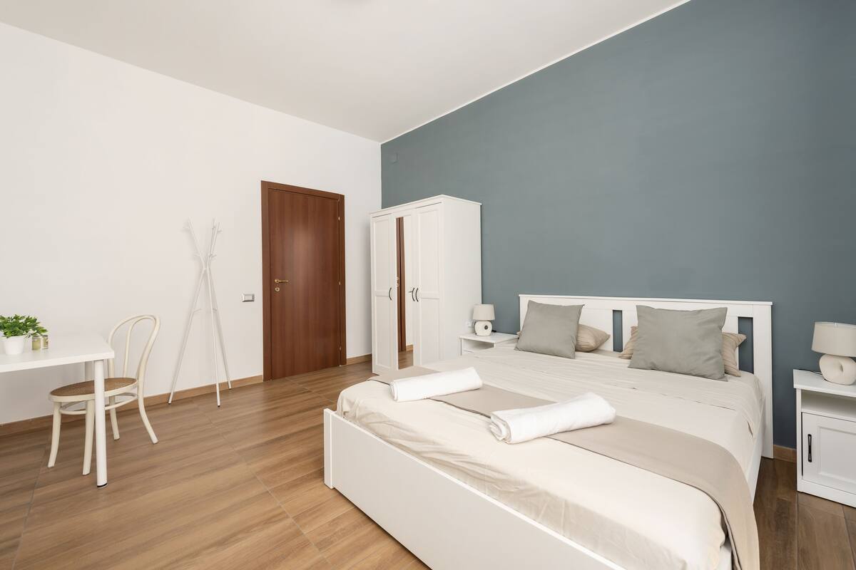A bedroom with a bed, bedside tables, a wardrobe, a desk, and a chair.