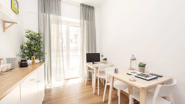 Een moderne, goed verlichte kamer met een houten bureau, witte stoelen, een computer en een potplant.